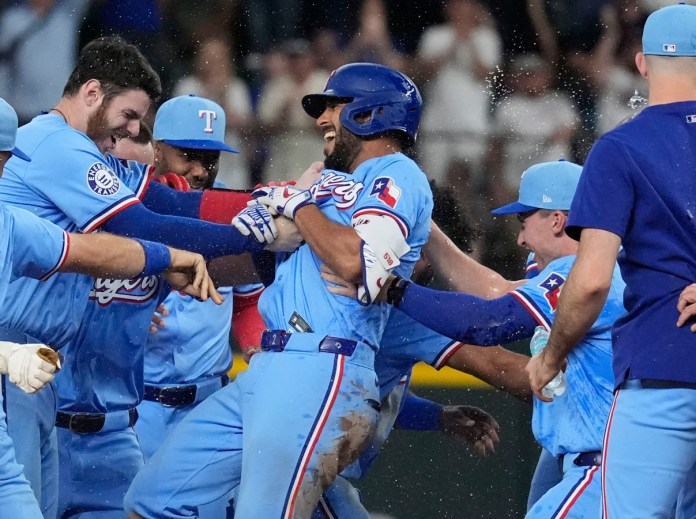 Marcus Semien (centro), de los Rangers de Texas, es felicitado por sus compañeros luego de conectar un sencillo que remolcó al dominicano Leody Taveras en el 9no episodio del juego de béisbol ante los Marineros de Seattle, el domingo 22 de septiembre de 2024, en Arlington, Texas. (AP Foto/LM Otero)