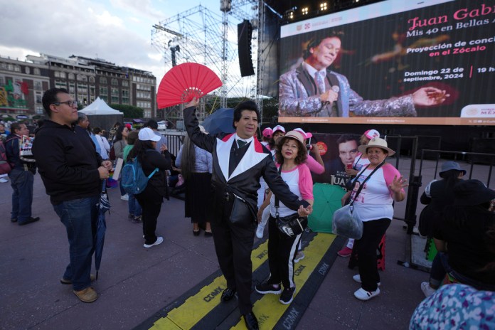 Jhoanfa "El Espejo de Juan Gabriel", un imitador del fallecido astro mexicano Juan Gabriel, actúa junto a un club de fans antes de la proyección de uno de los conciertos de Juan Gabriel en el Zócalo, la plaza principal de la Ciudad de México, el domingo 22 de septiembre de 2024.(Foto AP/Fernando Llano)