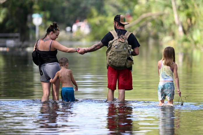 Dustin Holmes, segundo de derecha a izquierda, sostiene la mano de su novia, Hailey Morgan, mientras regresan a su vivienda inundada acompañados de sus hijos Aria Skye Hall, de 7 años, a la derecha, y Kyle Ross, de 4 años, tras el paso del huracán Helene, el 27 de septiembre de 2024, en Crystal River, Florida. (AP Foto/Phelan M. Ebenhack, Archivo)