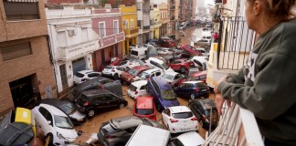 Una mujer mira por su balcón a los vehículos atrapados en la calle durante una inundación en Valencia, el miércoles 30 de octubre de 2024. (AP Foto/Alberto Saiz)