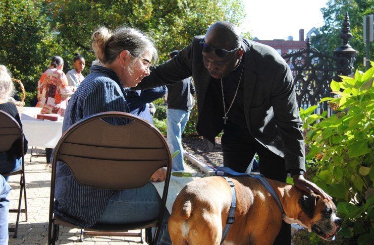 El reverendo Jean Beniste, un inmigrante haitiano, bendice a un perro y a su propietaria, el sábado 5 de octubre de 2024, durante el evento de Bendición de Animales en el jardín de la Iglesia Episcopal St. Paul de Concord, Nueva Hampshire. (G. Jeffrey MacDonald vía AP)