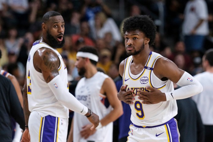 Bronny James (9), derecha, de los Lakers de Los Ángeles, entra a la cancha con su padre LeBron James (23), durante la primera mitad de un partido de pretemporada de baloncesto de la NBA el domingo 6 de octubre de 2024, en Palm Desert, California (Foto AP/William Liang)