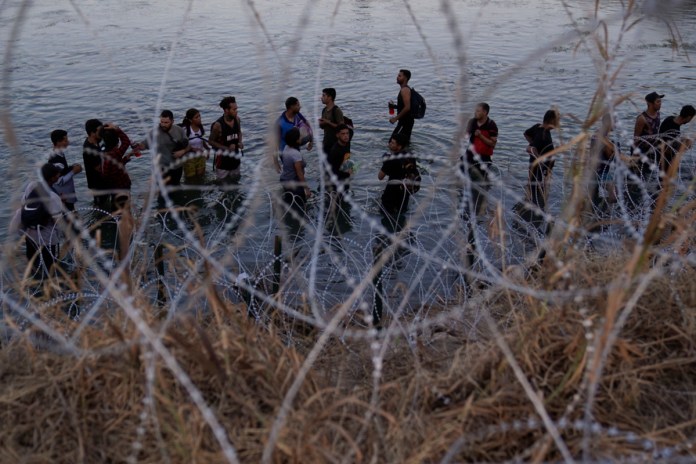 Migrantes esperan junto a una barrera de alambre de púas tras haber cruzado el rio Bravo (o Grande) desde el lado mexicano hacia Estados Unidos en Eagle Pass, Texas. Foto La Hora: AP