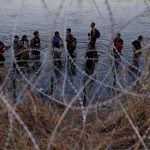 Migrantes esperan junto a una barrera de alambre de púas tras haber cruzado el rio Bravo (o Grande) desde el lado mexicano hacia Estados Unidos en Eagle Pass, Texas. Foto La Hora: AP