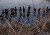 Migrantes esperan junto a una barrera de alambre de púas tras haber cruzado el rio Bravo (o Grande) desde el lado mexicano hacia Estados Unidos en Eagle Pass, Texas. Foto La Hora: AP