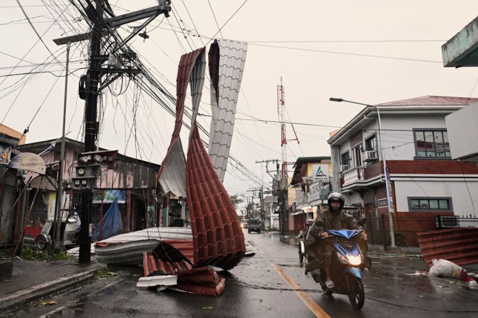 Un motorista pasa junto a un trozo de tejado colgado de cables eléctricos debido al tifón Man-yi, en una calle en el municipio de Baler, provincia de Aurora, en el nordeste de Filipinas, el lunes 18 de noviembre de 2024. Foto: La Hora/AP