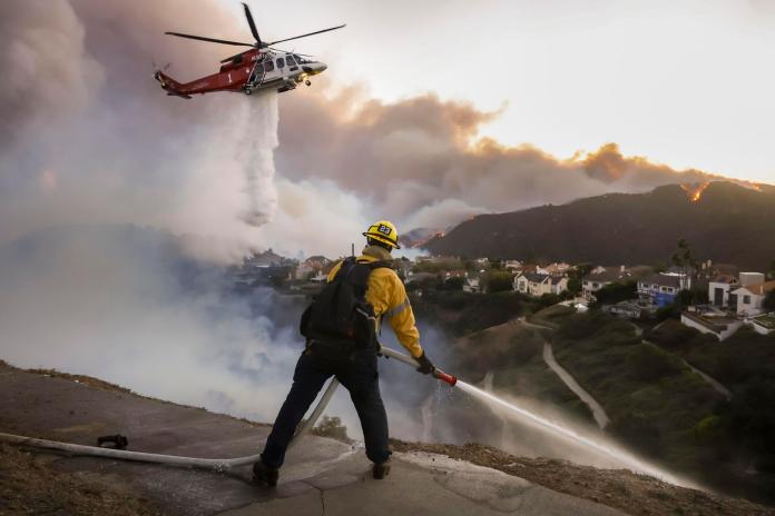 Los bomberos del condado de Los Ángeles utilizan mangueras y lanzan agua desde un helicóptero para combatir el incendio forestal de Palisades en Pacific Palisades, California, (EE.UU.). EFE/CAROLINE BREHMAN