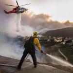 Los bomberos del condado de Los Ángeles utilizan mangueras y lanzan agua desde un helicóptero para combatir el incendio forestal de Palisades en Pacific Palisades, California, (EE.UU.). EFE/CAROLINE BREHMAN