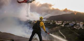 Los bomberos del condado de Los Ángeles utilizan mangueras y lanzan agua desde un helicóptero para combatir el incendio forestal de Palisades en Pacific Palisades, California, (EE.UU.). EFE/CAROLINE BREHMAN