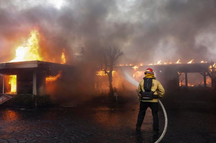 Los bomberos del condado de Los Ángeles utilizan mangueras y lanzan agua desde un helicóptero para combatir el incendio forestal de Palisades en Pacific Palisades, California, (EE.UU.). EFE/CAROLINE BREHMAN