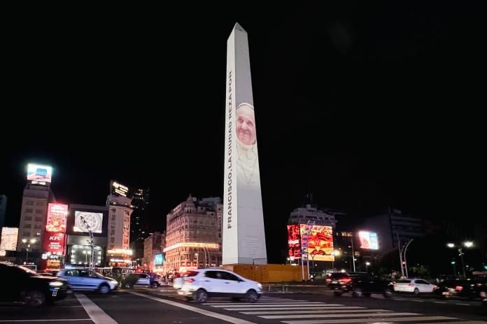 Fotografía del monumento El Obelisco iluminado con la imagen del papa Francisco y el mensaje 