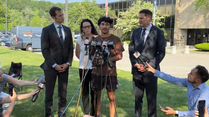 Marcelo Gomes da Silva, de 18 años, al centro, un estudiante de secundaria de Massachusetts que llegó a Estados Unidos cuando tenía 7 años de edad y fue detenido por agentes del Servicio de Inmigración y Control de Aduanas el sábado 31 de mayo de 2025, habla con la prensa después de ser liberado bajo fianza, acompañado de los representantes Seth Moulton, un demócrata por Massachusetts, a la derecha, y Jake Auchincloss, también demócrata del estado, el jueves 5 de junio de 2025, en Burlington, Massachusetts. (AP Foto/Rodrique Ngowi)