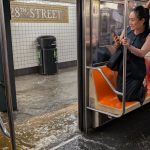 Usuario del metro de Nueva York se refugian sobre sus asientos ante inundaciones reportadas el 14 de julio por la noche.