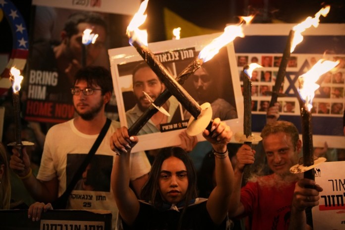 Manifestantes portan antorchas durante una protesta para exigir la liberación inmediata de todos los rehenes retenidos por Hamás en la Franja de Gaza, y para pedir el fin de la guerra, el jueves 7 de agosto de 2025, frente a la oficina del primer ministro en Jerusalén. (AP Foto/Ohad Zwigenberg)