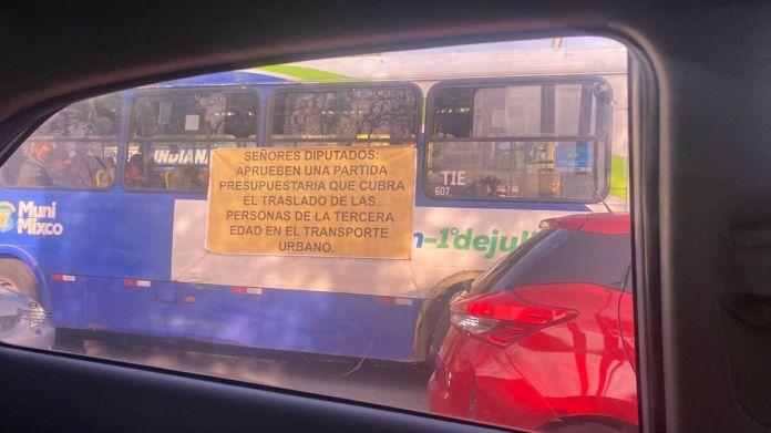 Manta vinílica con exigencias por pago de servicio gratuito de transporte al adulto mayor.
