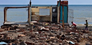 Personas caminan frente a una casa destruida, este jueves en el poblado de Guamá, Santiago de Cuba. Foto La Hora: EFE