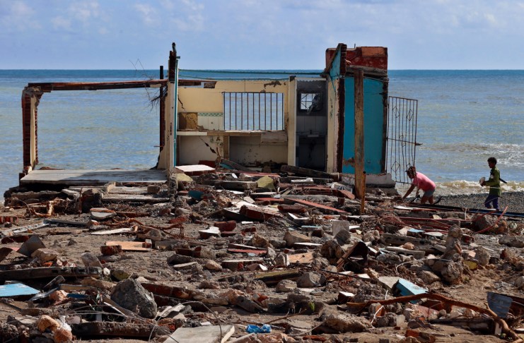 Personas caminan frente a una casa destruida, este jueves en el poblado de Guamá, Santiago de Cuba. Foto La Hora: EFE