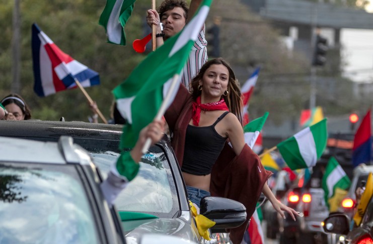 Personas sostienen banderas de diferentes partidos políticos de Costa Rica este domingo, en la fuente de la Hispanidad en San José.