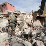 Un brigadista y un perro rescatistas inspeccionan en los escombros de un edificio que colapsó por los terremotos, en La Guaira, Venezuela. Foto: EFE.