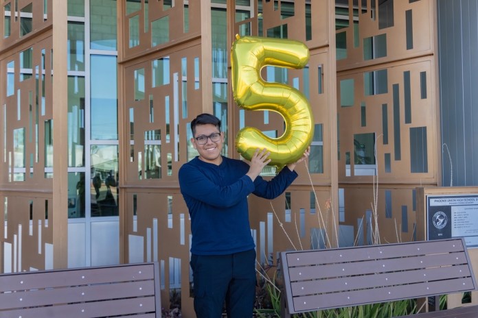 Fotografía divulgada por el Distrito de Escuelas Secundarias Phoenix Union donde aparece Joseph Parra Miguel, de 18 años e hijo de inmigrantes mexicanos, sosteniendo un globo en forma del número cinco en alusión a su logro de 5 millones de dólares en becas.