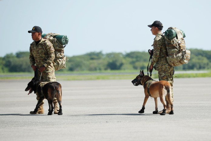 Dos rescatistas acompañados de perros de rescate se preparan para viajar a Venezuela este jueves, en las instalaciones de la Base Área Militar en San Luis Talpa. El Salvador. Foto La Hora: EFE 