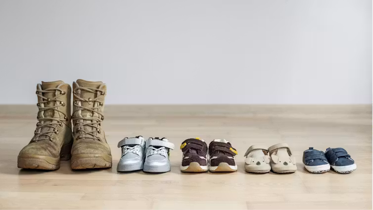 Un par de botas de adulto seguidas por varios zapatos de niños