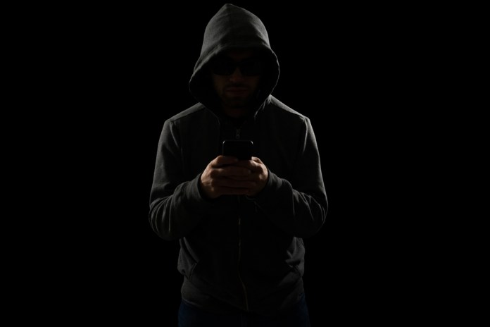 Dangerous,Scammer,With,A,Hoodie,Texting,On,The,Smartphone,And Como un impuesto obscuro, la extorsión se añade a los costos y precios que pagan los consumidores. Foto La Hora: Shutterstock
