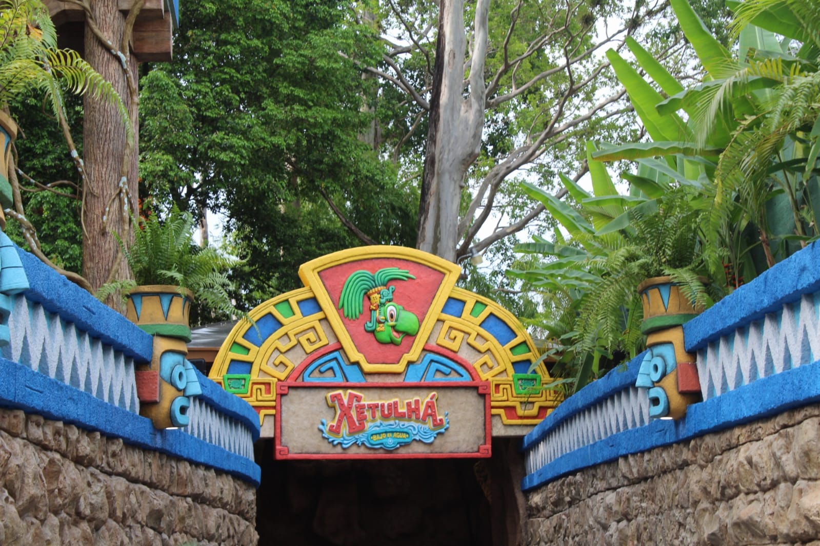 Una entrada a un pasillo subterráneo que muestra la arquitectura inspirada en los mayas, con el nombre de Xetulhá y árboles arriba.