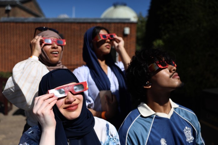LONDON (United Kingdom), 12/08/2026.- People shield their eyes with protective glasses during an eclipse event at Greenwich Observatory in London, Britain, 12 August 2026. A solar eclipse is when the Moon passes in front of the Sun and blocks its light. In London, more than 90 percent of the Sun was obscured at the peak of the eclipse. The eclipse occurred in the UK from 18:17 to 20:06, reaching its peak at 19:12. (Reino Unido, Londres) EFE/EPA/NEIL HALL