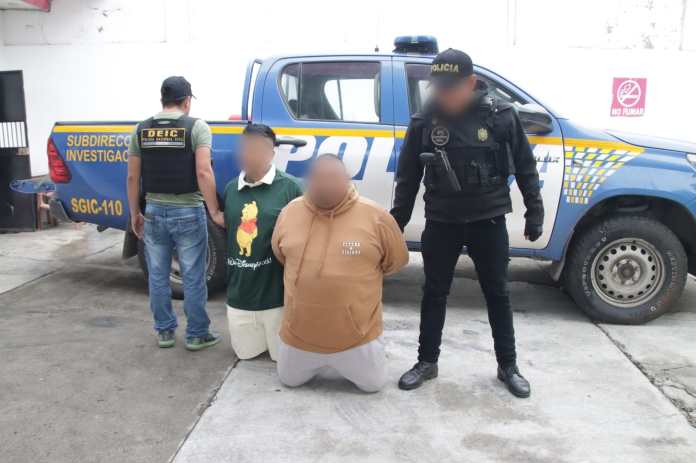 Los dos detenidos permanecen arrodillados junto a agentes de la PNC tras el operativo en Santa Elena Barillas, Villa Canales.
