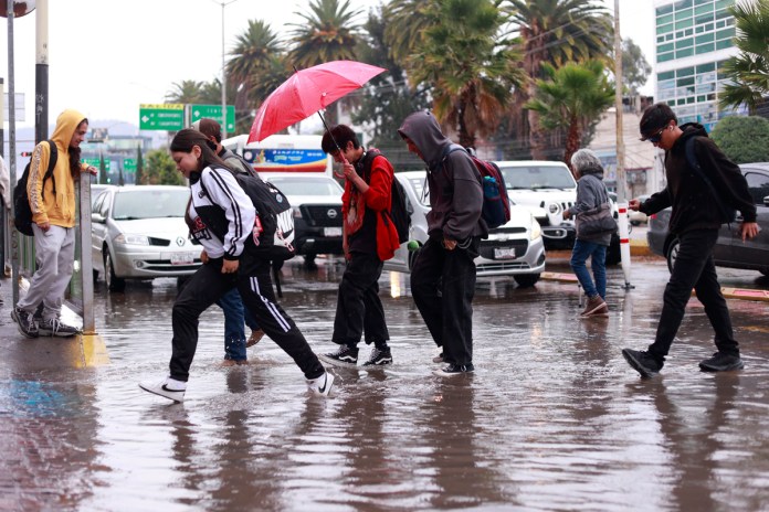 Personas caminan por una calle inundada debido a las fuertes lluvias en Pachuca (México) por tormenta tropical. Foto La Hora: EFE