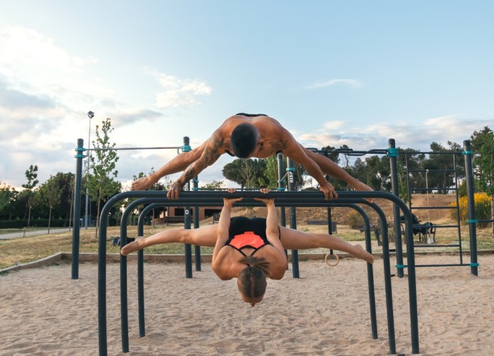 Couple,Training,Together,In,A,Calisthenics,Park.,Doing,Back,Lever Entrenando juntos en un parque de calistenia, haciendo palanca trasera y planche a caballo.
